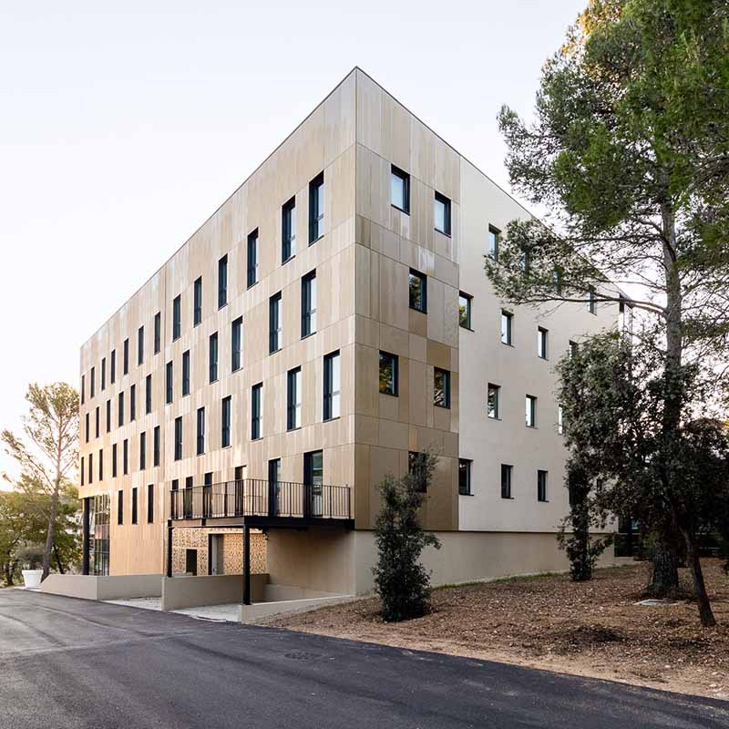 Photographe bureaux Marseille : façade moderne d'un bâtiment tertiaire au design géométrique, bordé de pins sous un ciel clair.
