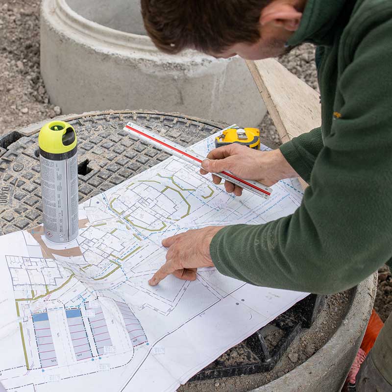 photographe chantier Marseille Photographe BTP Marseille : gros plan d'un chef de chantier vérifiant un plan de masse sur un regard en béton.