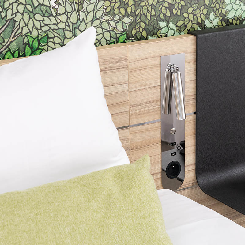 Photographe hôtel Marseille : détail tête de lit en bois, liseuse chromée et papier peint floral, décoration chambre pro.