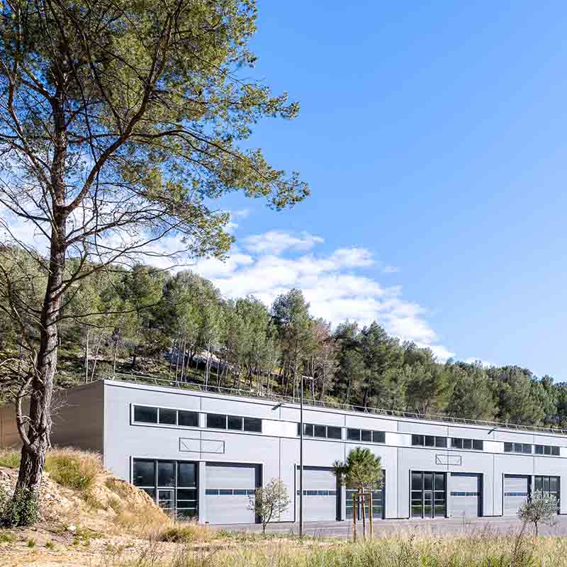 Photographe architecture Marseille : hangar industriel moderne en lisière de forêt, bâtiment tertiaire gris et baies vitrées.