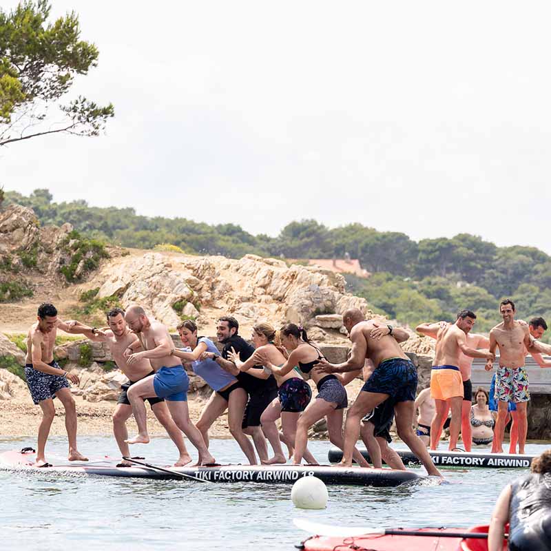 photo evenement entreprise team building marseille Photo team building Marseille : collaborateurs en maillot de bain s'amusant sur une planche de paddle géante en pleine mer.