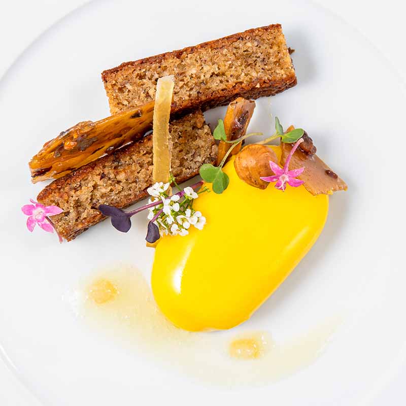 photo plat culinaire gastronomique marseille Photographie culinaire d'un dessert moderne avec mousse mangue, cake aux noisettes et fleurs sur une assiette blanche.