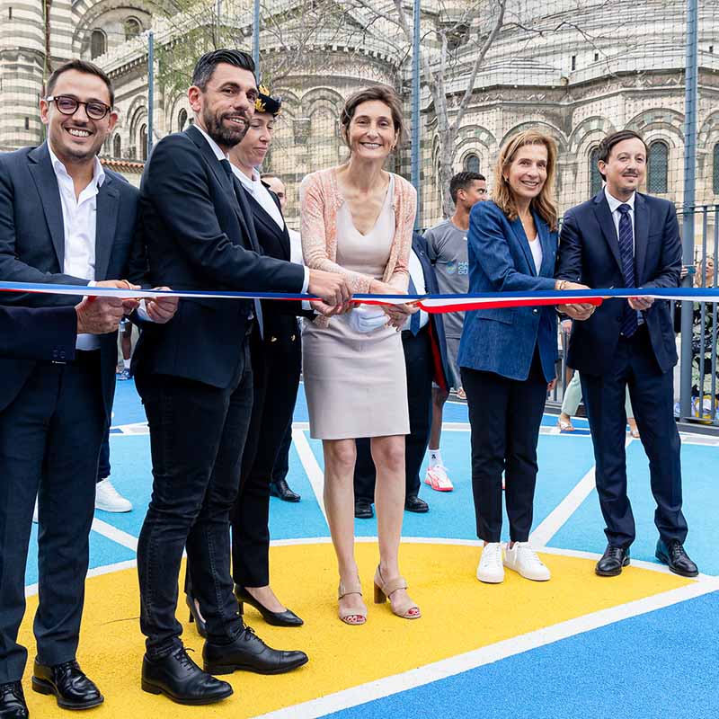 Photo événementielle Marseille : inauguration d'un stade avec découpe du ruban tricolore par des élus devant une cathédrale.