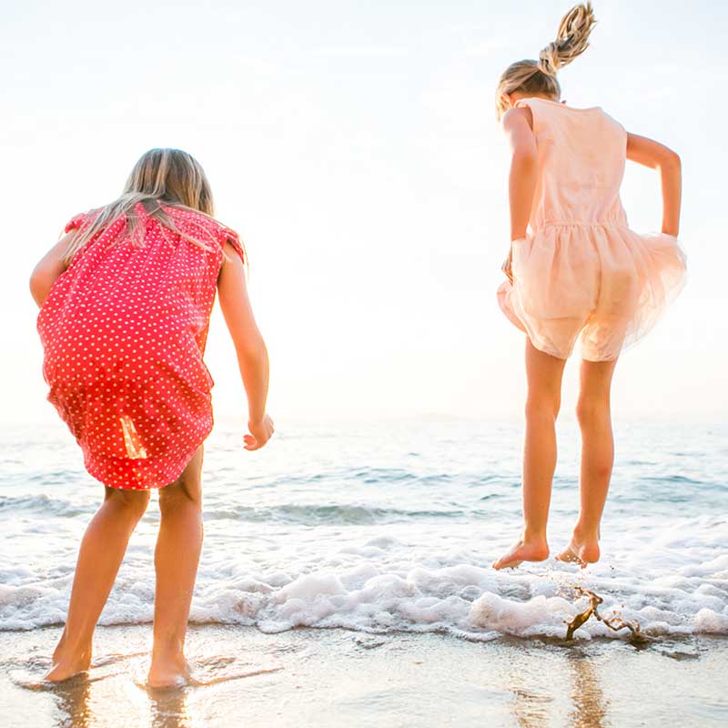 Photographe famille Marseille : deux fillettes sautant avec joie dans les vagues au soleil couchant en PACA.
