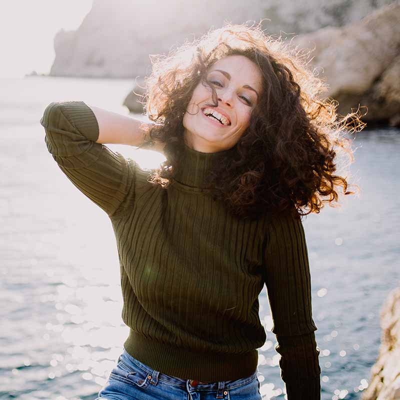 Photographe portrait Marseille : jeune femme brune pétillante face à la mer Méditerranée au soleil couchant.