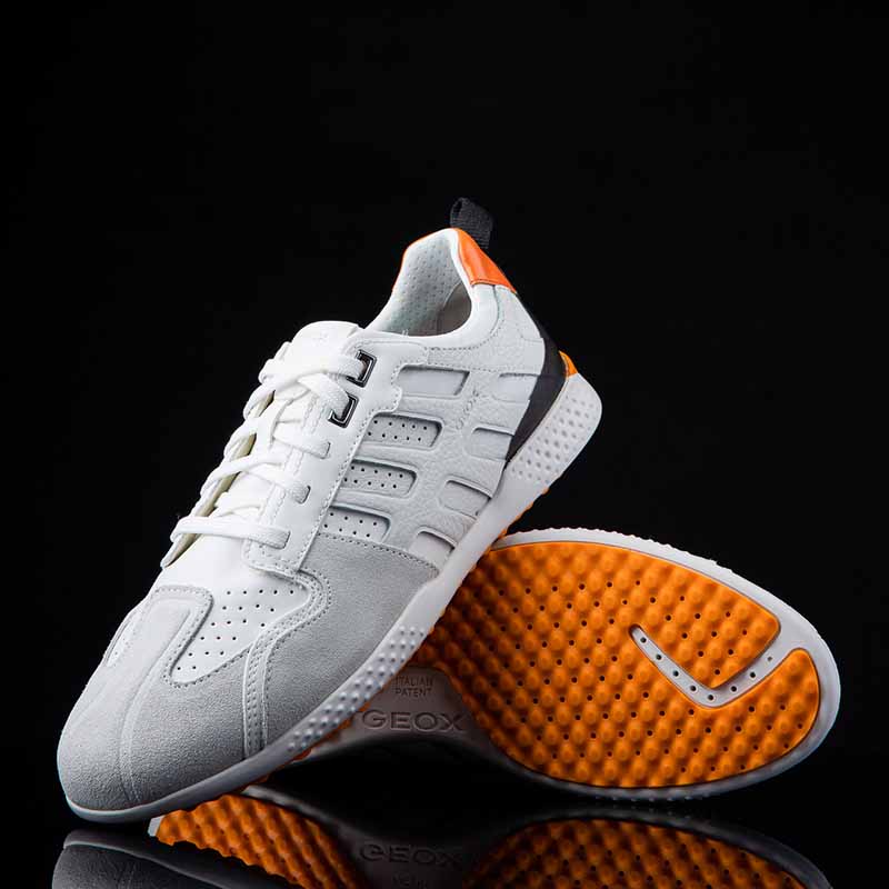 photographe produit marseille Photographie packshot de baskets Geox blanches et grises avec semelle orange dynamique sur fond noir, reflet élégant.