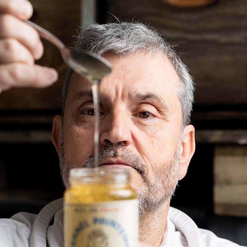 photographe reportage agriculture apiculteur marseille Photo agriculture Marseille : portrait d'un apiculteur barbu versant du miel doré dans un pot lors d'une récolte locale.