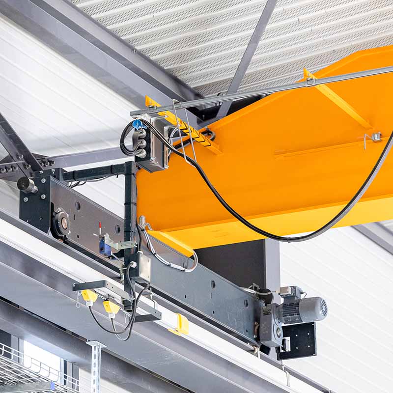 photographe reportage industriel marseille Photo industrielle Marseille : détail technique d'un pont roulant de levage jaune et gris installé sous la charpente d'un dépôt.