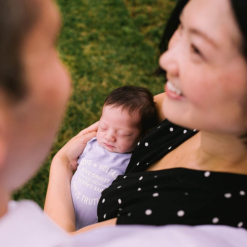 Photographe famille Marseille : maman tenant son bébé endormi et regardant son mari dans un jardin en PACA.