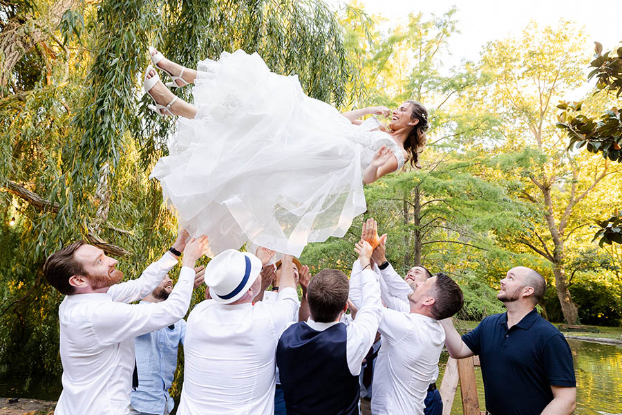 La mariée en robe blanche lancée en l'air par ses témoins masculins dans un parc à Marseille lors d'un moment festif.
