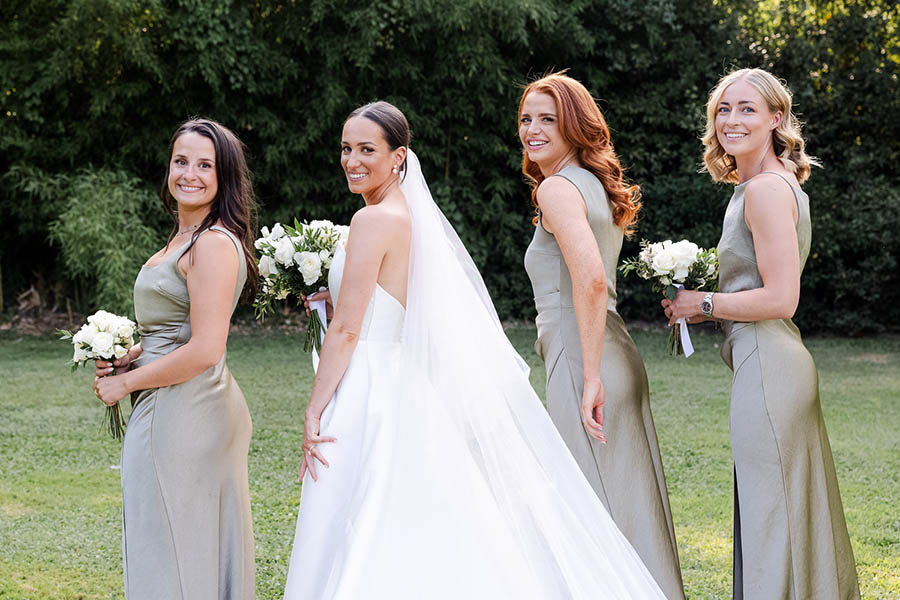 La mariée en robe blanche et ses trois témoins en robes de satin vert sauge marchant dans un parc verdoyant à Marseille.